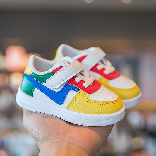 Colorful toddler sneakers with velcro straps, pastel pink, red, yellow, and mint accents, held in hand