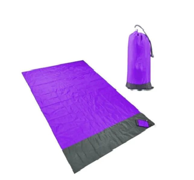 Mandotos sandproof portable beach mat spread out on sandy beach with colorful towel and blue sky.