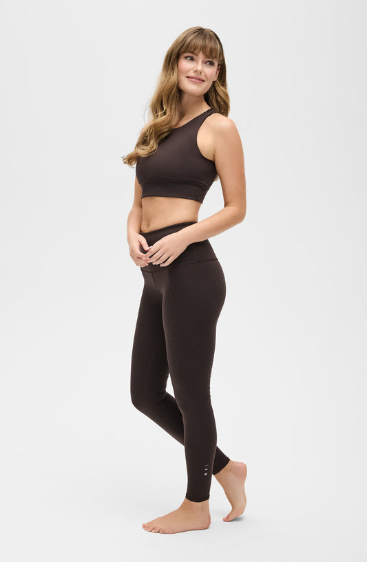 Woman in dark brown seamless sports bra and high-waisted leggings with subtle dot texture, ideal for yoga or gym workouts.