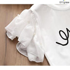 White ruffle sleeve t-shirt with pearl buttons and black script design, laid on wood surface