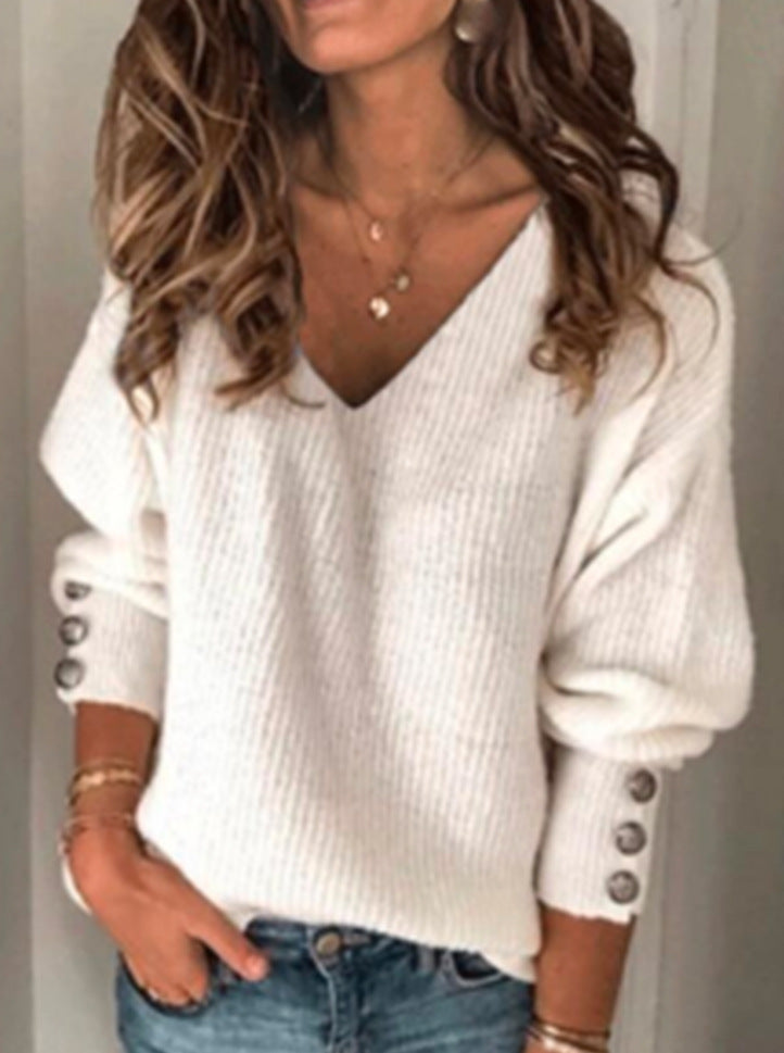 Woman wearing a chic white V-neck knit sweater with buttoned cuffs and blue jeans.