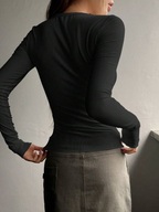 Back view of a woman wearing a black ribbed long-sleeve Mandotos International tee and grey skirt.