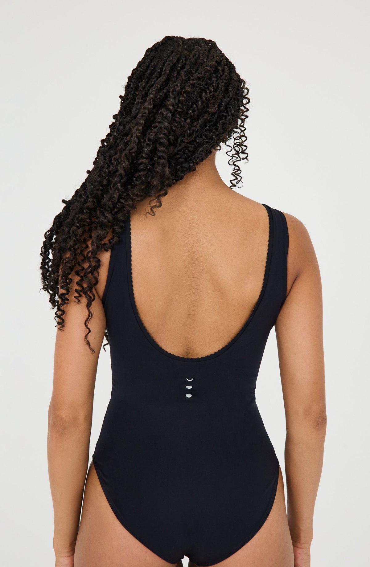 Black one-piece swimsuit with low back and moon phase details, worn by woman with curly hair