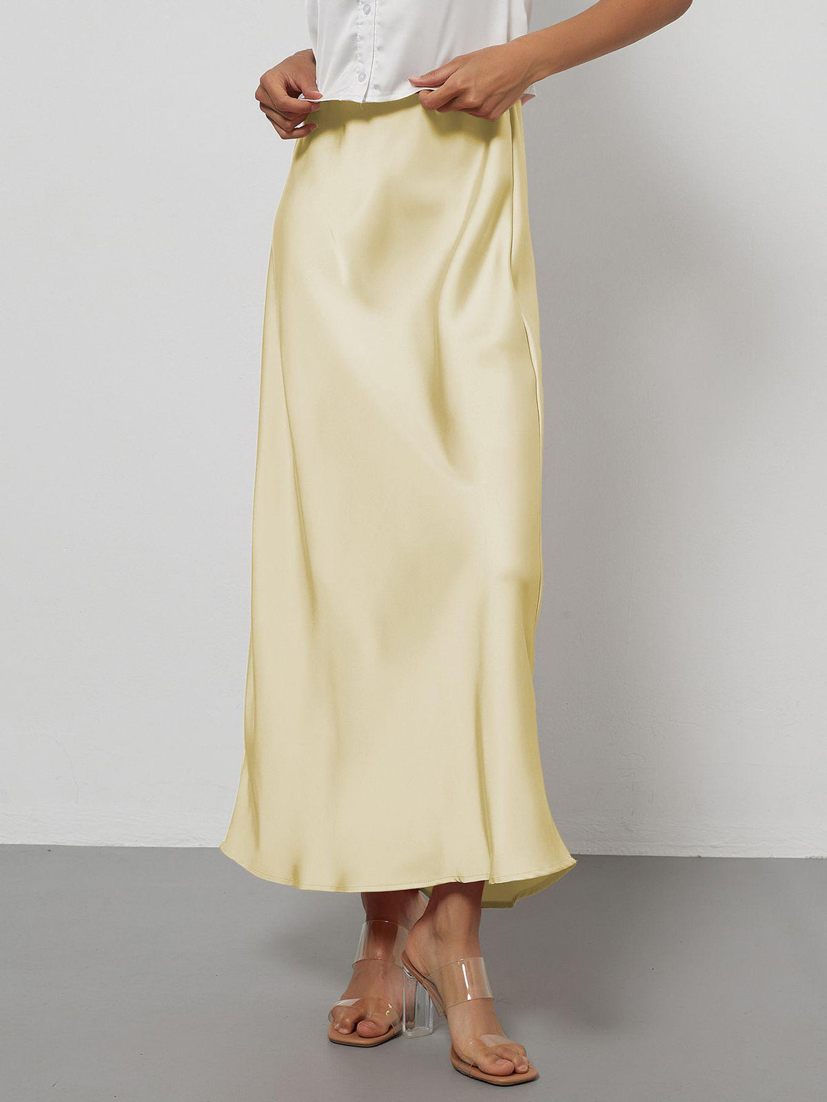 Elegant pale yellow satin midi skirt with a slim flowy fit worn with clear heels.