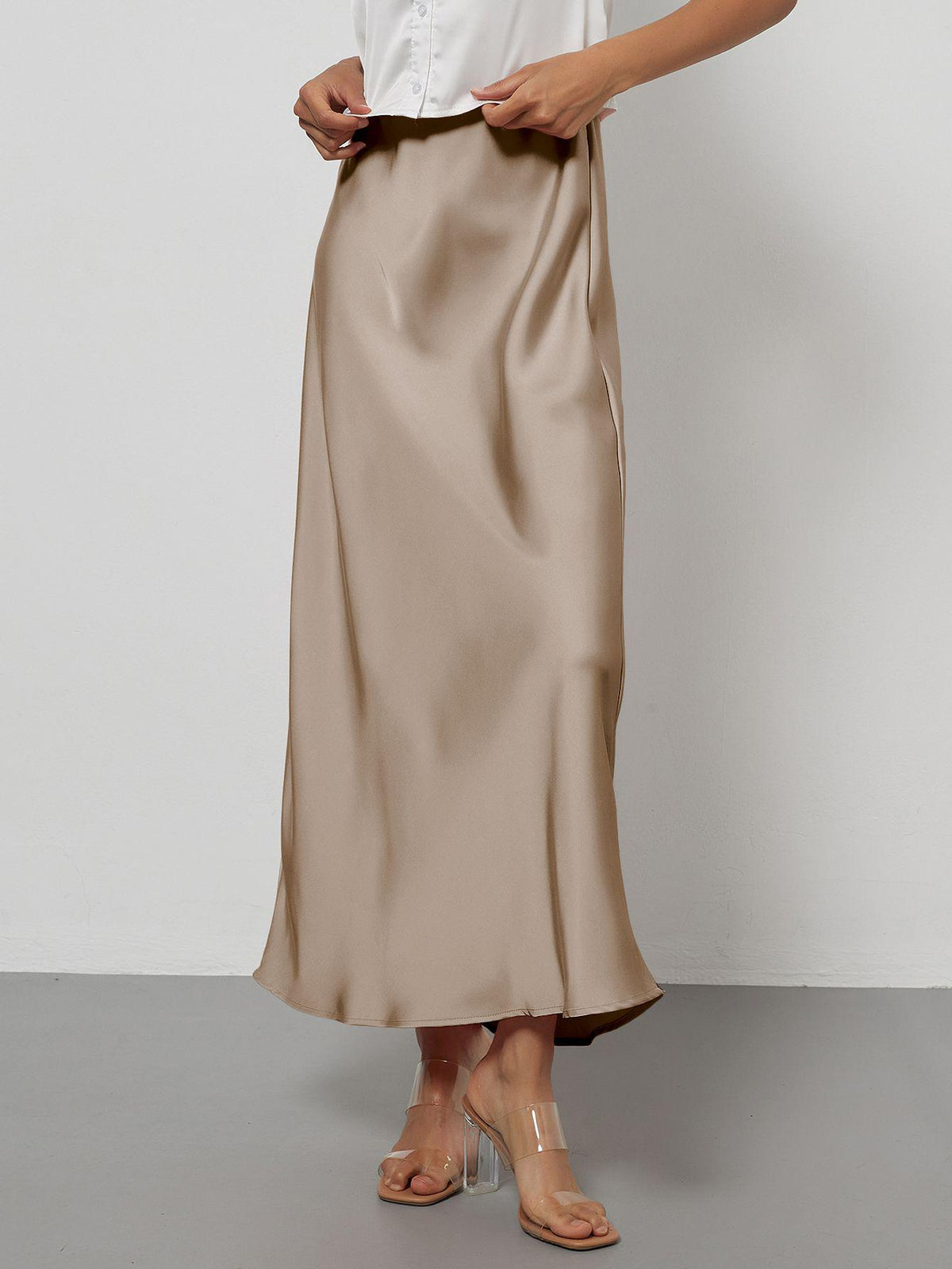 Elegant champagne satin midi skirt with a slim flowy fit paired with clear heels.