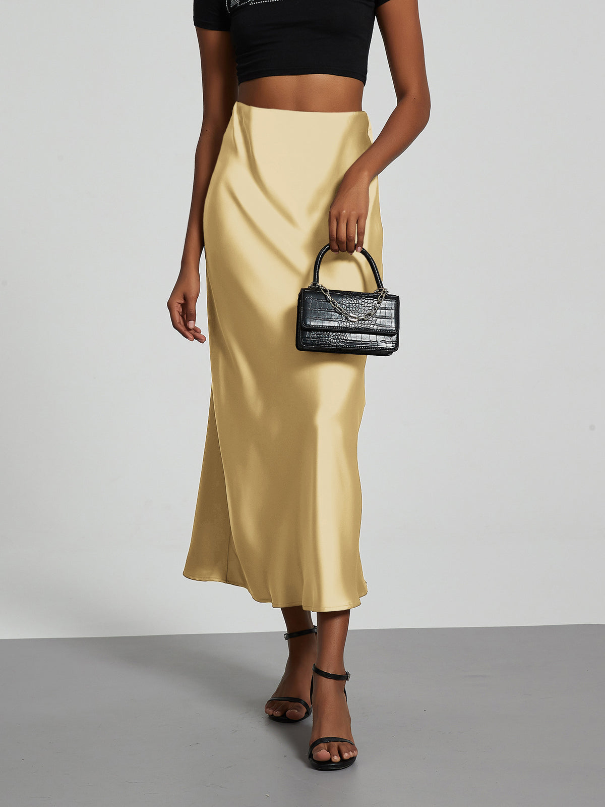 Elegant champagne satin midi skirt paired with a black crop top and small crocodile handbag.