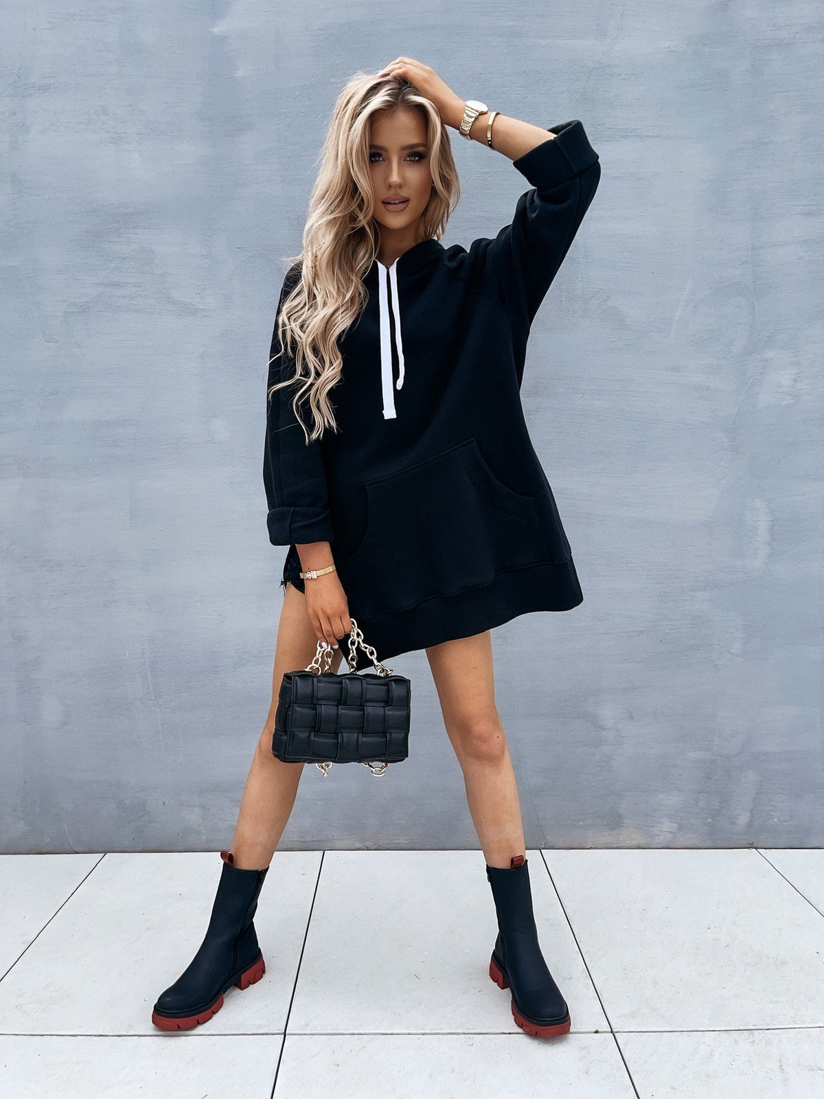 Woman wearing a black Mandotos International hooded pullover sweater and black boots.
