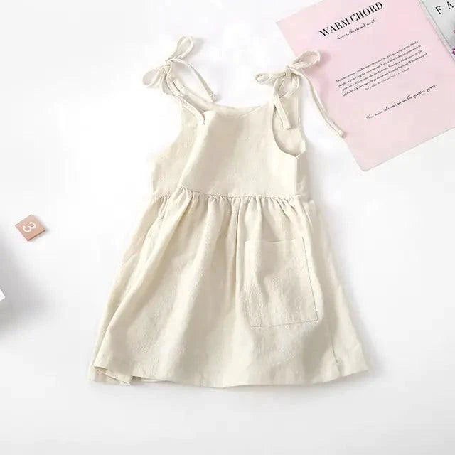 Toddler girl wearing a white cotton chic sundress by MANDOTOS, with ruffled straps and floral embroidery, outdoors in sunlight.