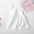 Toddler wearing a light cotton sundress with floral pattern, pink and white, from MANDOTOS, perfect for warm weather.